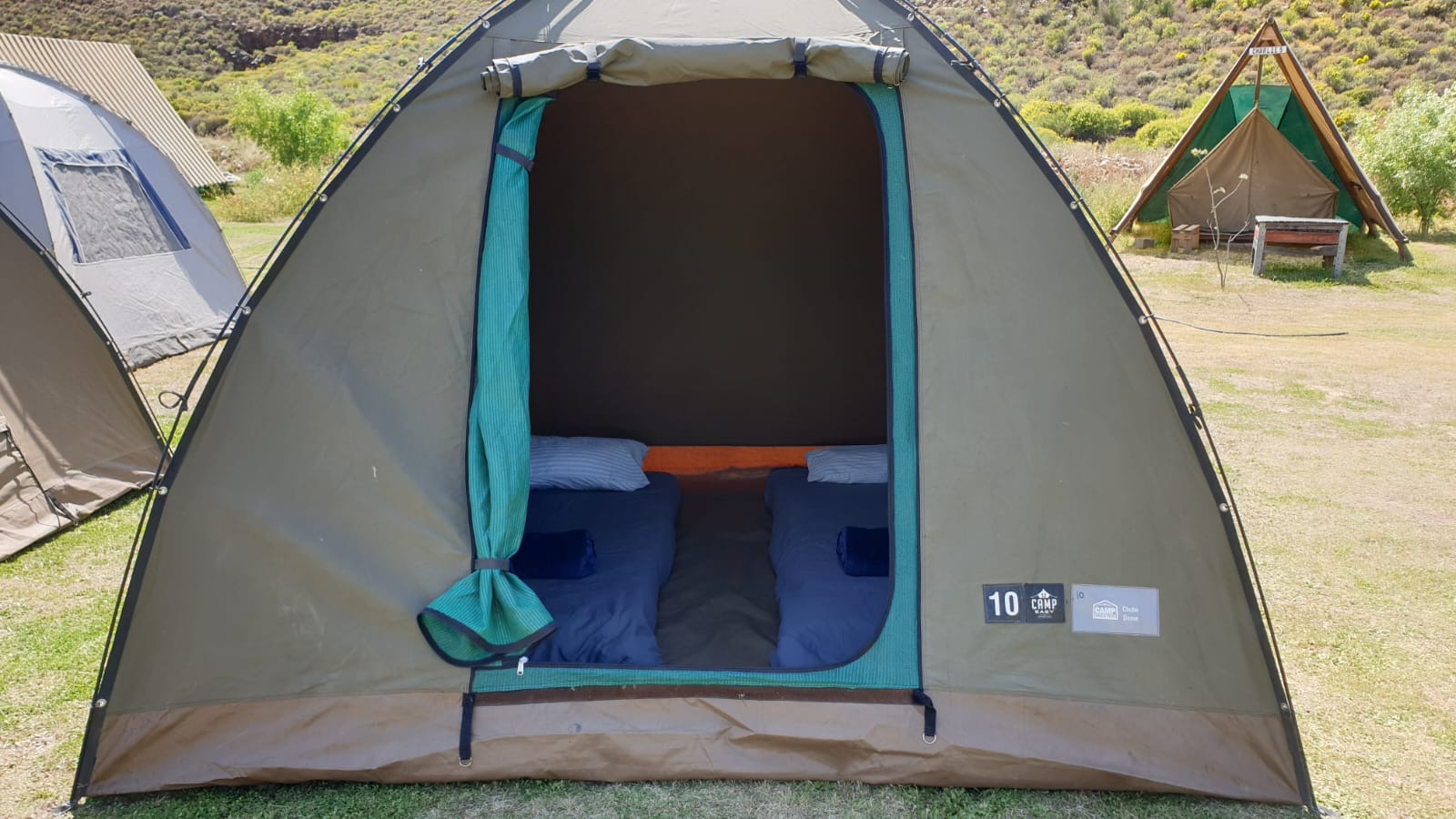 Inside a canvas glamping tent: two made-up mattresses with pillows and comforters
