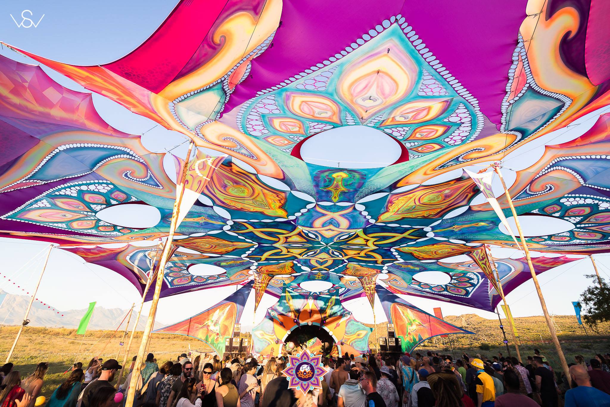 Dancers under a painted shade canopy at Earthdance, mountains behind