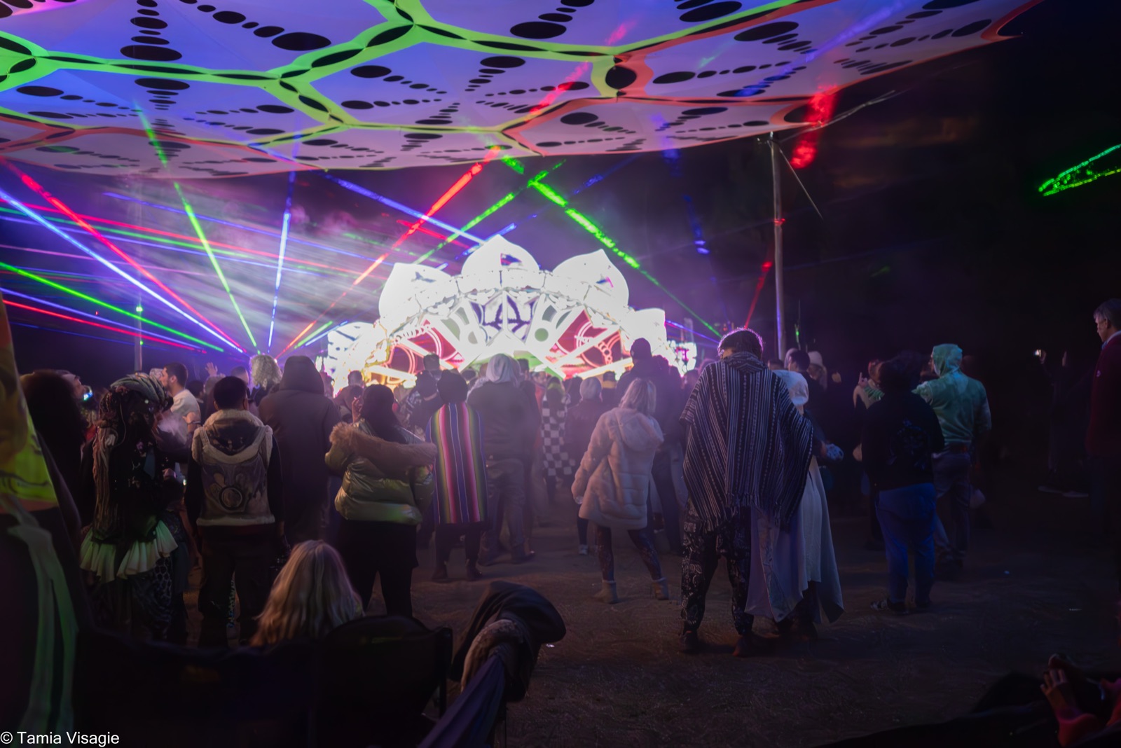A crowd standing together on the dancefloor at night as lasers cross a glowing stage