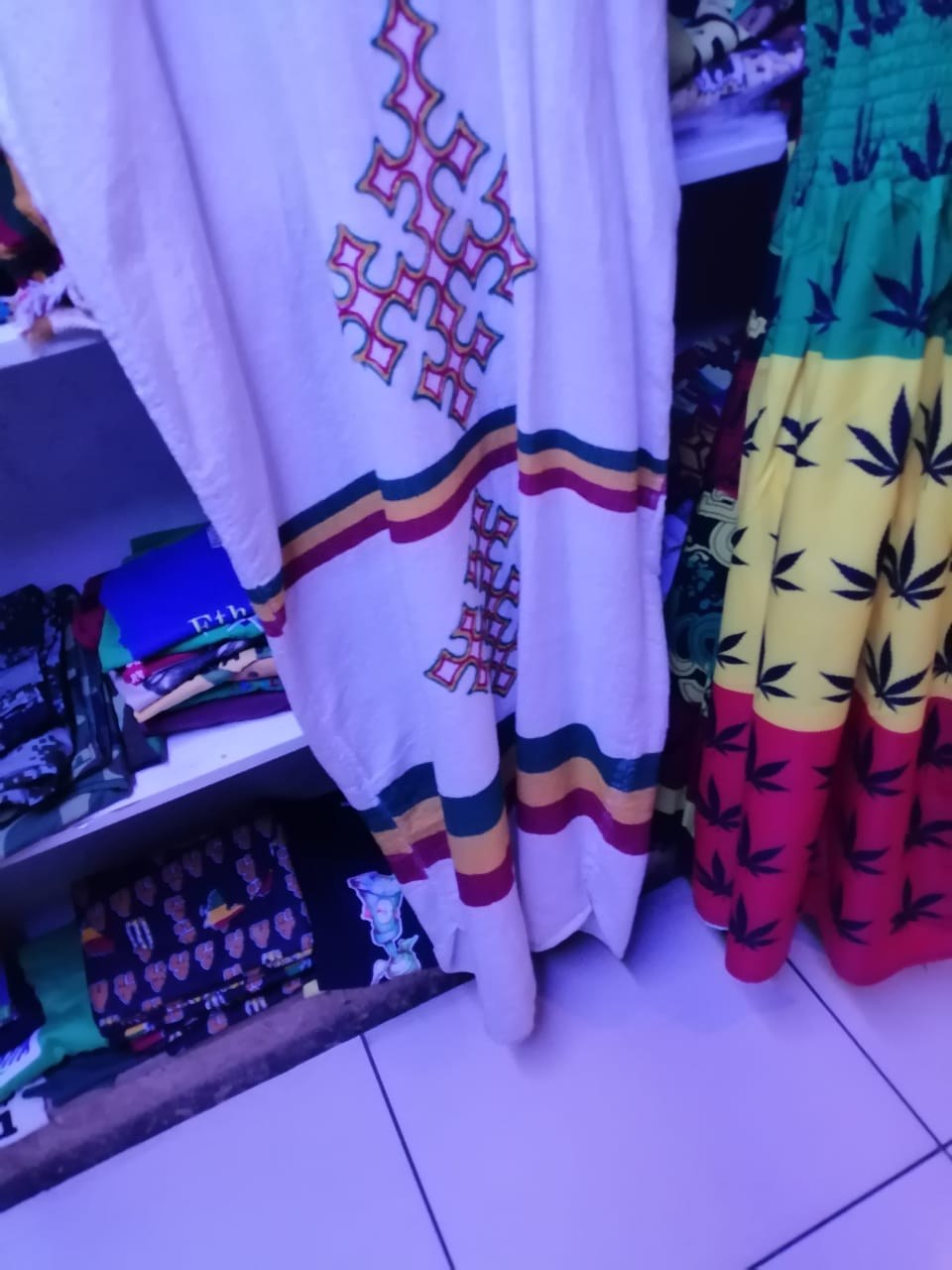 An embroidered white garment beside a green, yellow and red cannabis-leaf print dress