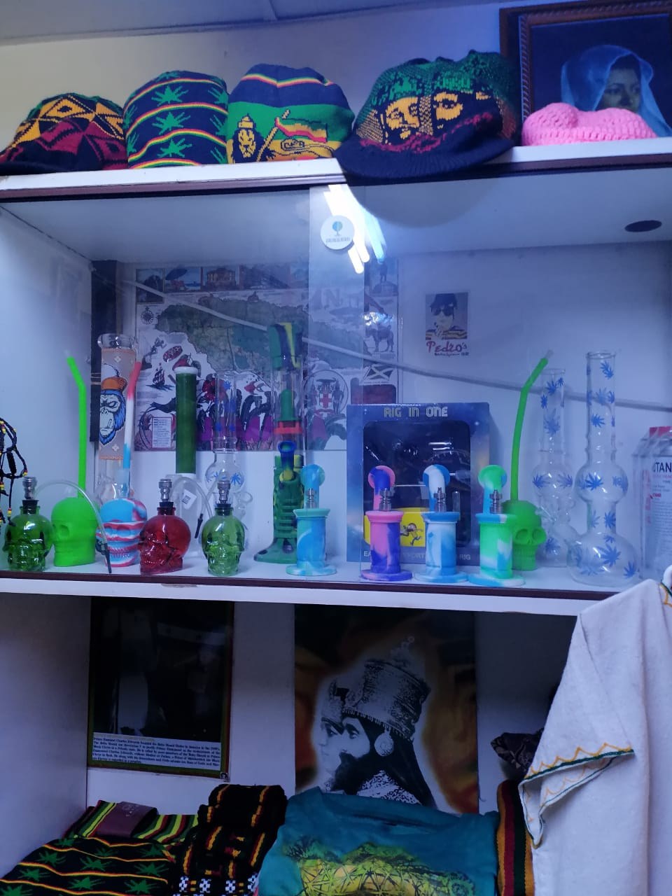Rasta-print beanies on a shelf above a display case of pipes and bongs