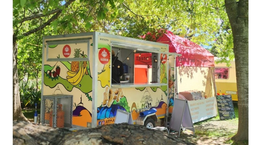 The colourful Atma food trailer under the trees, with fruit and city artwork painted on the side