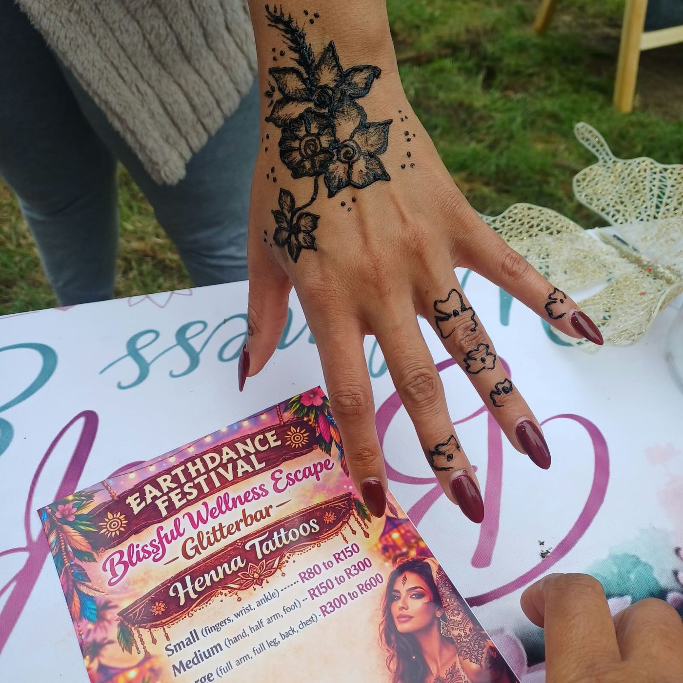 Henna art on a hand, held above the henna and glitter bar price card