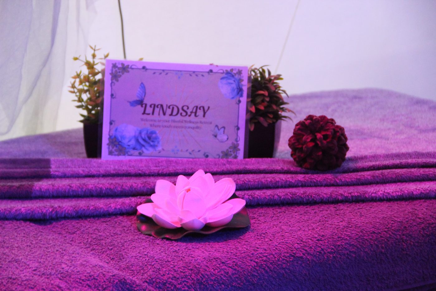 A pink lotus candle and a name card on folded purple towels