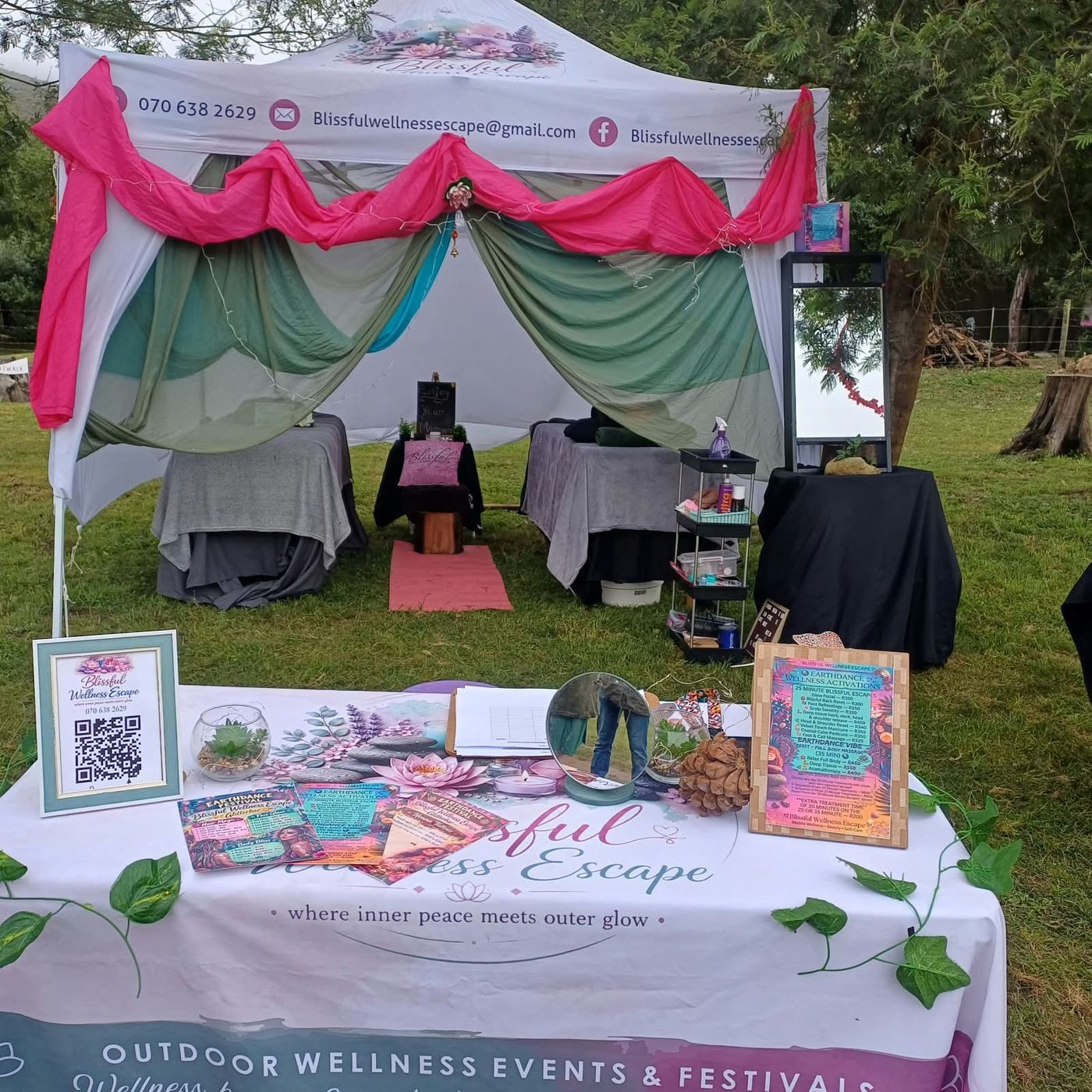 The Blissful Wellness Escape gazebo draped in pink and sage, with price cards and flyers on the front table