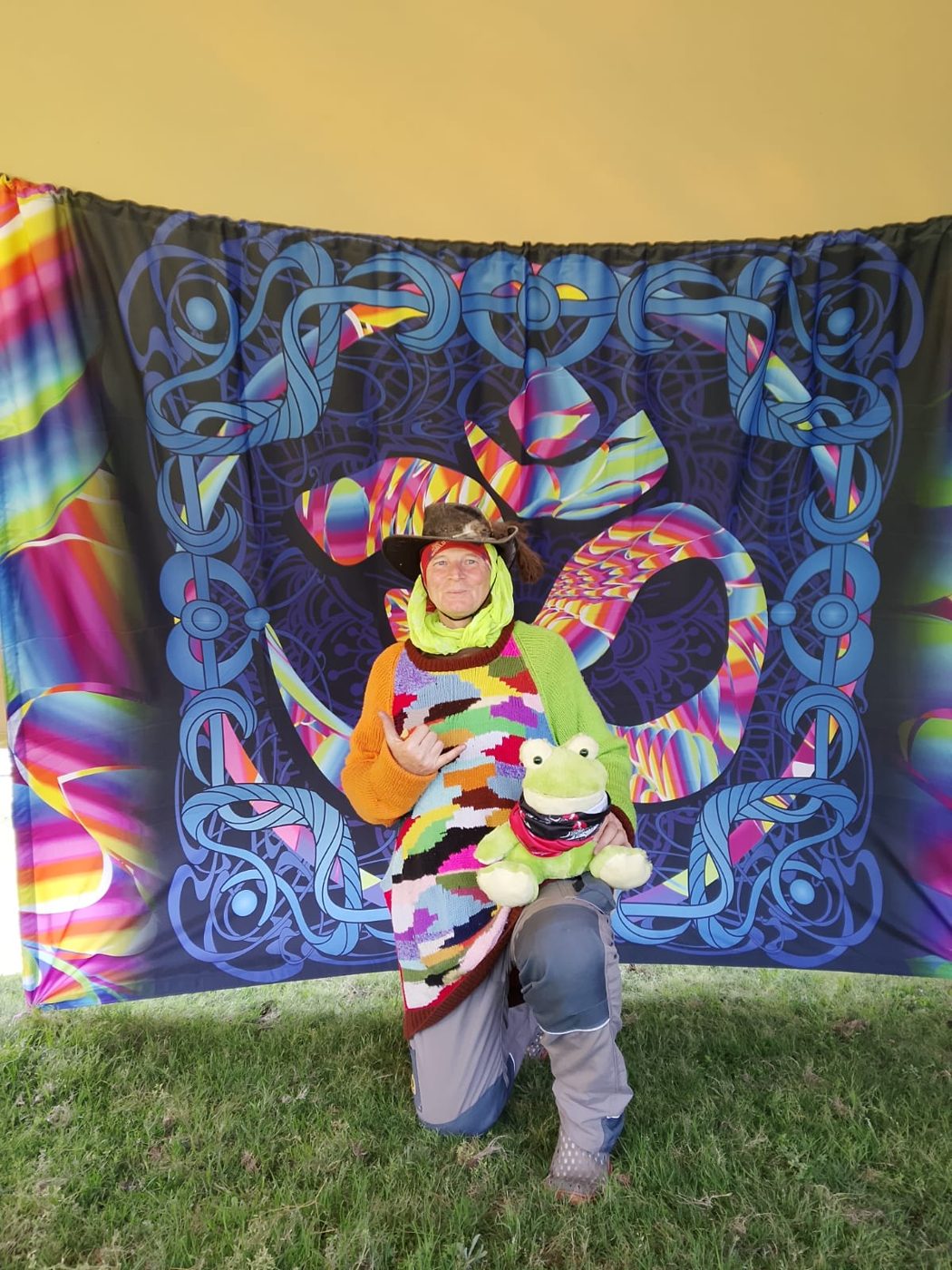 The Chill and Charge host kneeling in front of a psychedelic Om backdrop, holding a plush frog