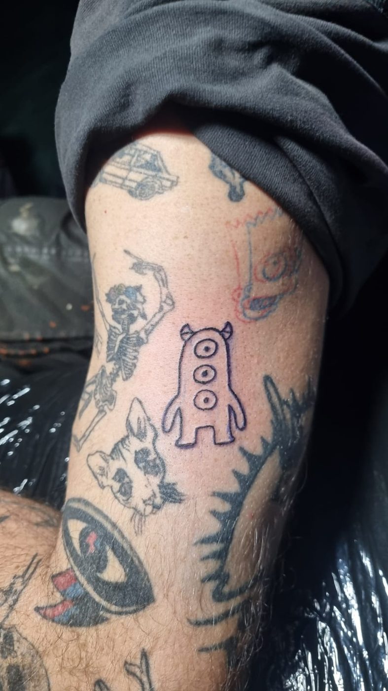 A tattooed arm with a small linework monster with three eyes among older pieces