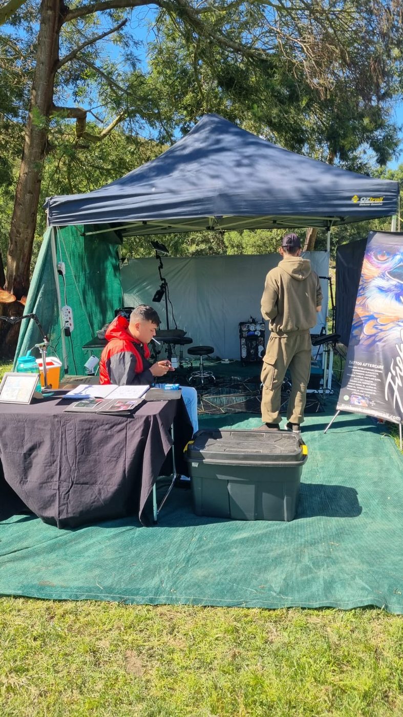 The Firehawk Ink stall under a navy gazebo on green matting, with the team at work