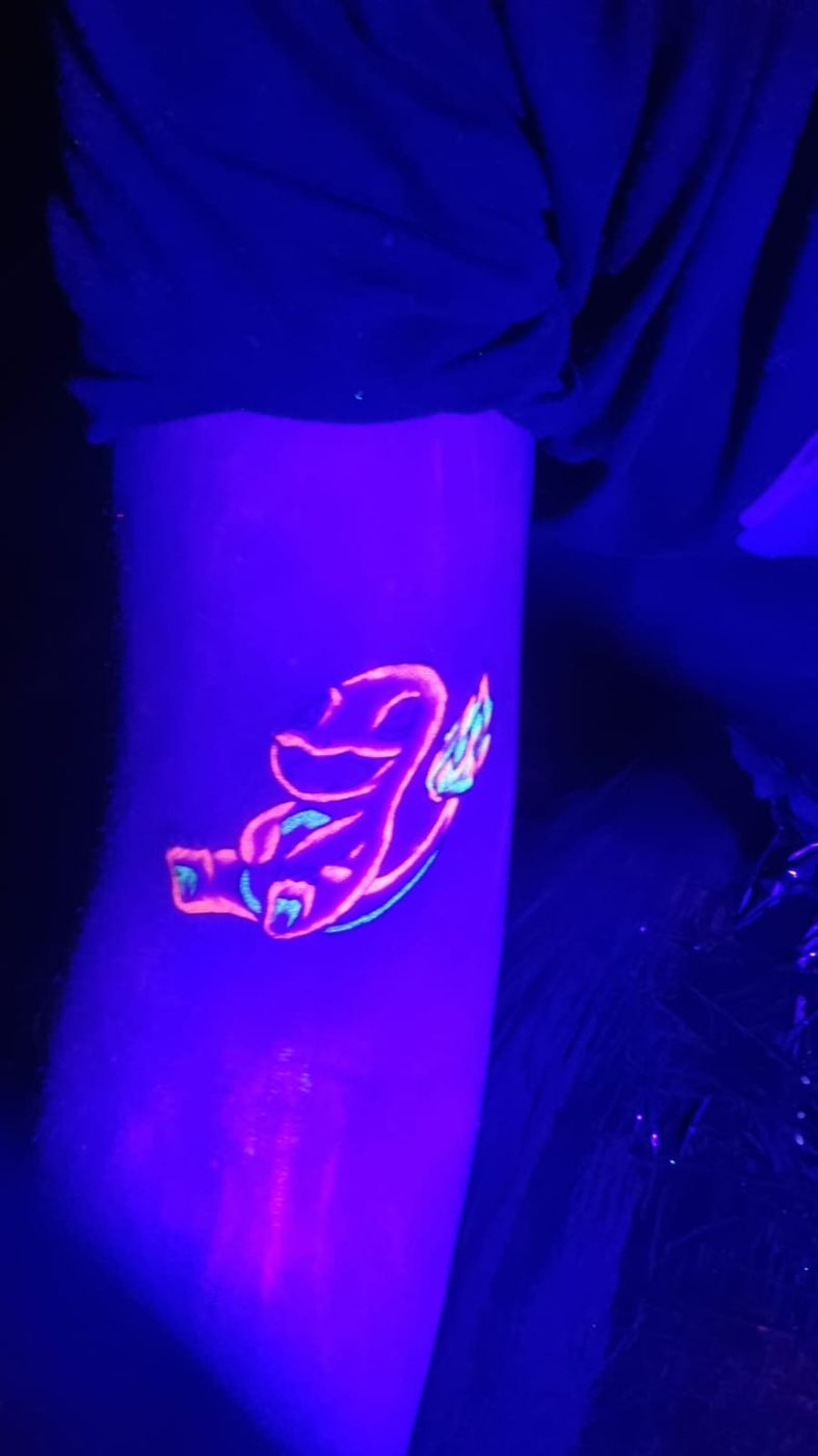 A UV tattoo of a pink hawk glowing under blacklight on a forearm