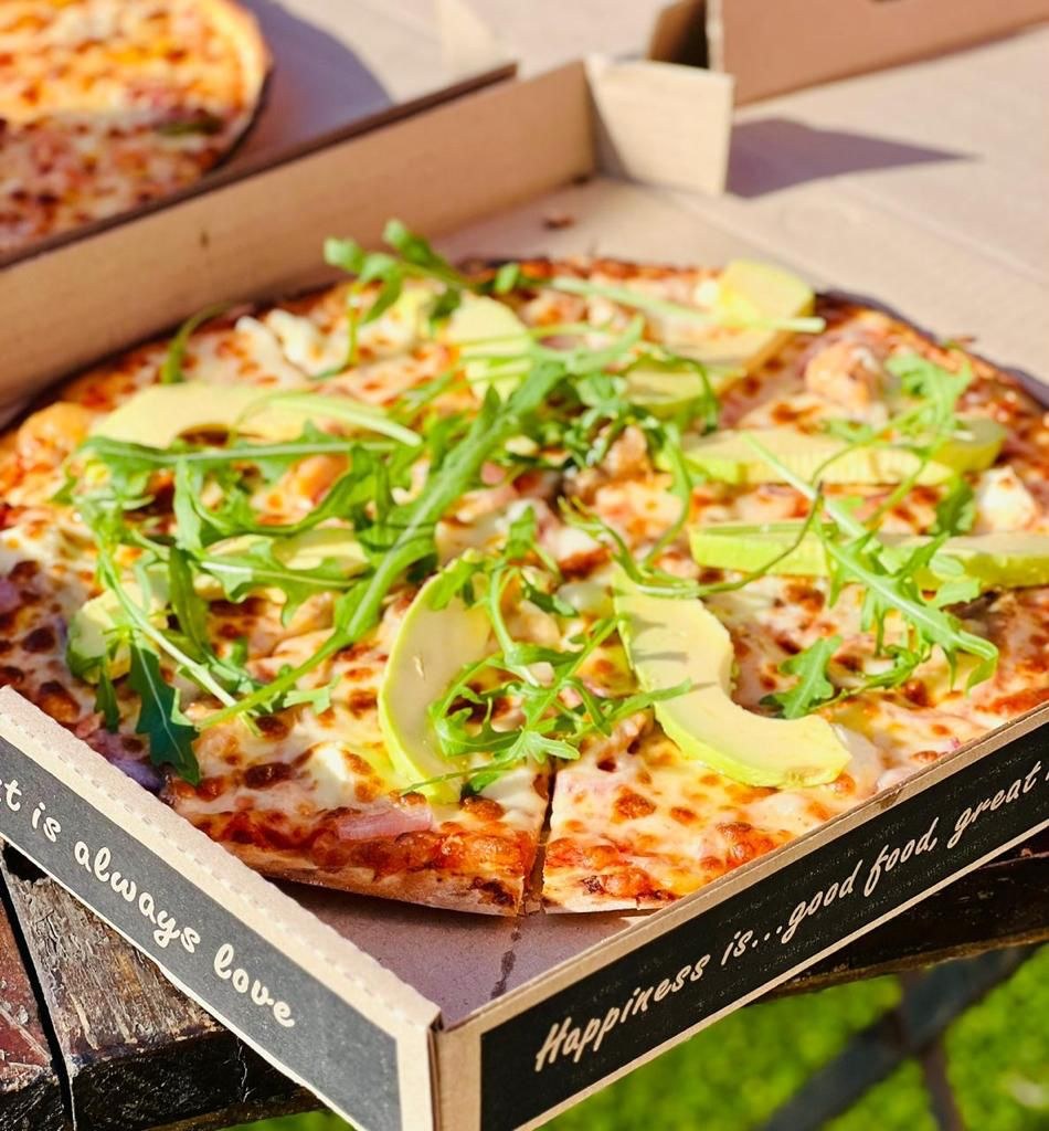 A pizza topped with rocket and avocado in a Love Pizza box