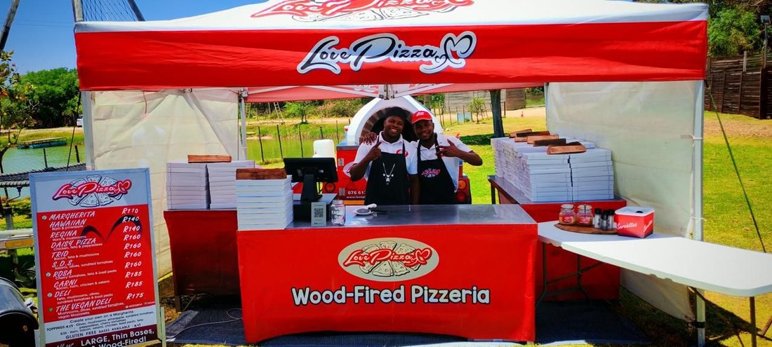 The Love Pizza stall, with a wood-fired oven, menu board and two staff serving
